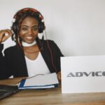 A cheerful woman in headphones providing online advice via laptop at her office desk.
